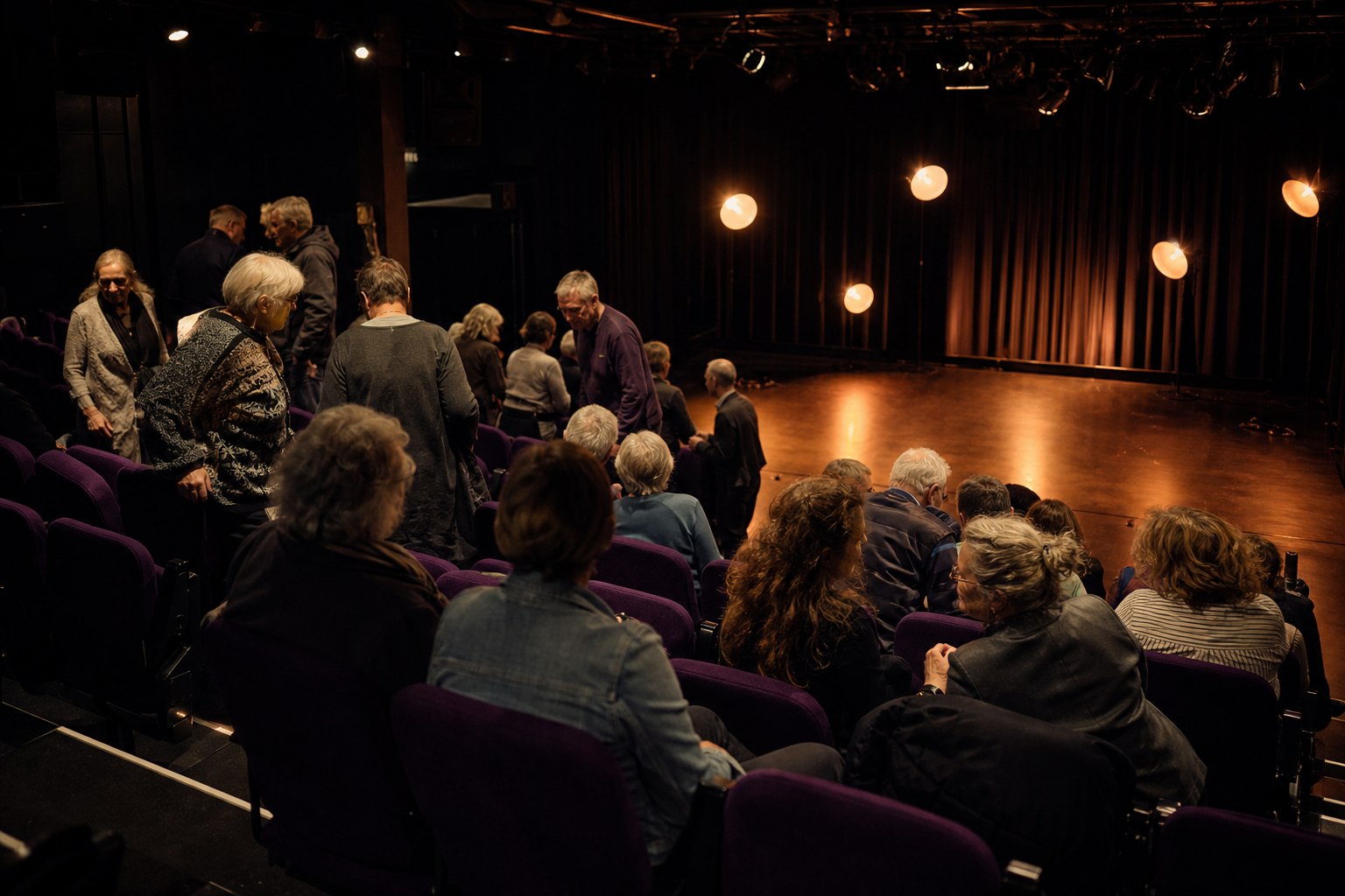 Publiek zoekt een zitplaats in een intiem theater met een leeg koperkleurig verlicht podium