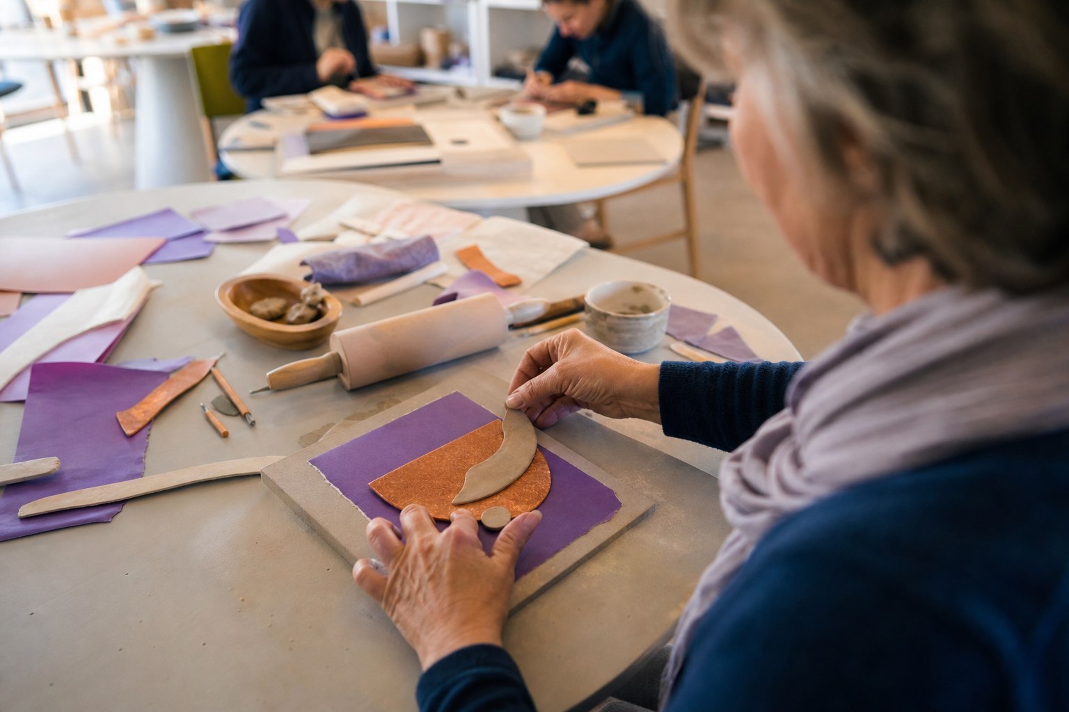 Deelnemer maakt aan een ronde werktafel een abstract relief van paars papier en koperkleurige klei